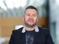Uśmiechnięty mężczyzna w czarnej marynarce i t-shircie z nadrukiem. Ciekawe, ile zarabia Norbi w Kole Fortuny?