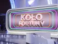 Na scenie studia telewizyjnego widnieje napis "KOŁO FORTUNY" otoczony neonami. To miejsce, gdzie marzenia o wygranej stają się rzeczywistością.
