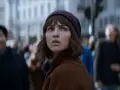 Młoda kobieta w brązowym płaszczu i bordowej czapce patrzy w górę, otoczona tłumem. Czy to zapowiedź netflix nowości dzisiaj?