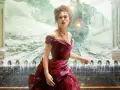 Anna Karenina w bordowej sukni, na tle pędzącego pociągu i śnieżnego krajobrazu. Obok stoją mężczyźni w strojach z epoki.