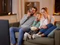 Rodzina ogląda filmy familijne, zajadając popcorn. Radość i wspólne chwile na kanapie.