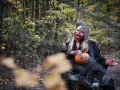 Kobieta w makijażu jack-o'-lantern trzyma dynię, gotowa na noc pełną **horrorów Netflix** w jesiennym lesie.