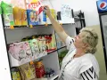 Kobieta wybiera przekąski w sklepiku szkolnym. Widać wafle ryżowe, granole i napoje. Co można kupić w sklepiku szkolnym? Prawie wszystko na szybką przekąskę!