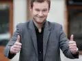 Krzysztof Wójcik z "Milionerów" pokazuje kciuki w górę, uśmiechając się.