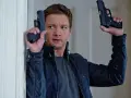Jeremy Renner w akcji, jakiego znamy z jego filmów i seriali. W rękach trzyma dwa pistolety, gotowy do strzału.