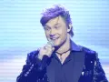 Jaka to melodia piosenkarze: przystojny mężczyzna z fioletowymi włosami śpiewa do mikrofonu w błyszczącej marynarce.