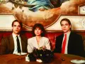 Jeremy Irons w filmach, tutaj z dwiema kobietami, siedzi przy stole w eleganckiej restauracji.