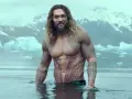 Jason Momoa w wodzie, z tatuażami, jak w filmach i serialach. W tle góry i lód.