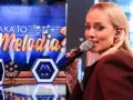 Jan Radwan śpiewa w programie "Jaka to melodia?". Na scenie widać neonowe dekoracje i logo programu.