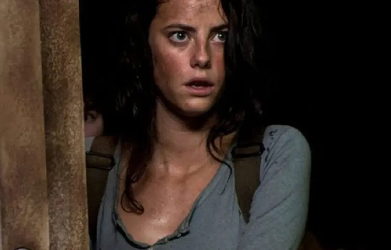 Twarz Kaji Scodelario, aktorki znanej z filmów i seriali, z przerażeniem w oczach, w ciemnym otoczeniu.