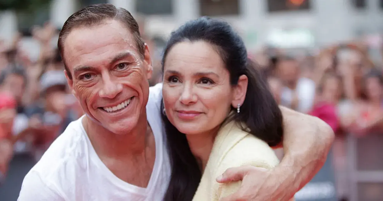 Jean-Claude Van Damme z uśmiechem obejmuje swoją żonę, Gladys Portugues, na tle tłumu.
