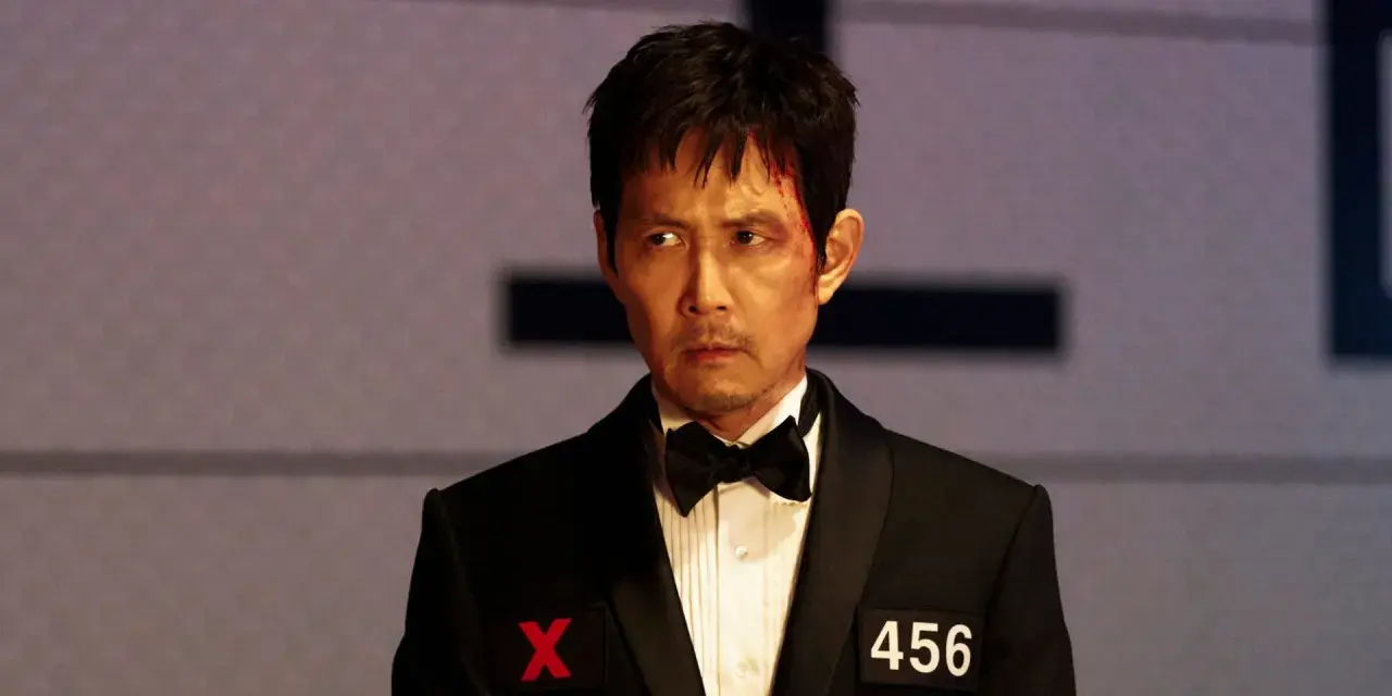 Zraniony Seong Gi-hun w garniturze z numerem 456 i symbolem X, gotowy na kolejne wyzwania w Squid Game sezon 4.