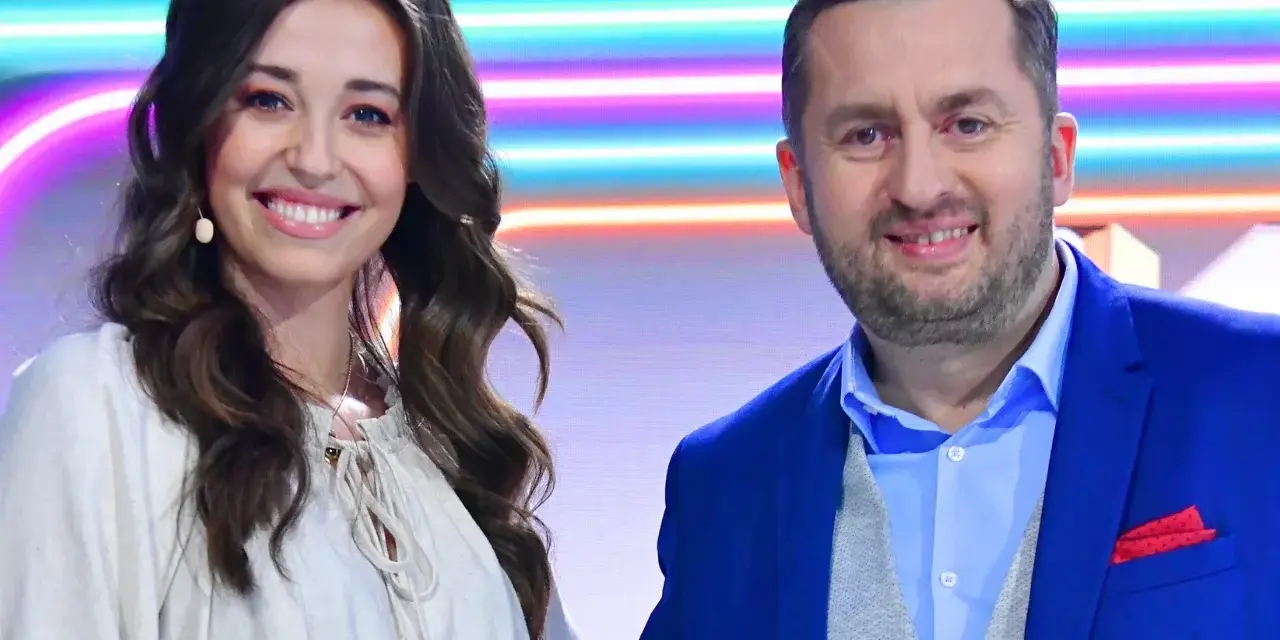 Uśmiechnięci prowadzący "Koła Fortuny" - ona w luźnej, ecru bluzce, on w niebieskiej marynarce i kamizelce.