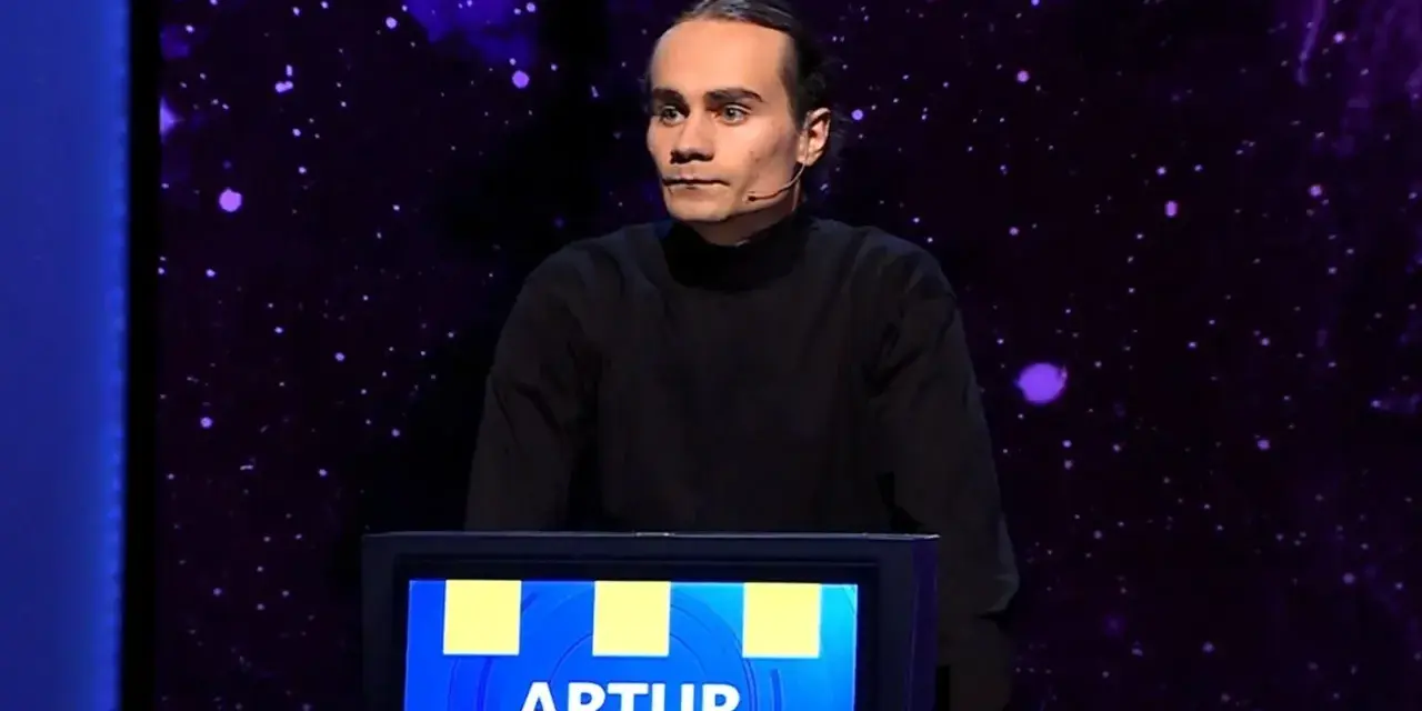 Artur, który wygrał jeden z dziesięciu, stoi na scenie w czarnym golfie.