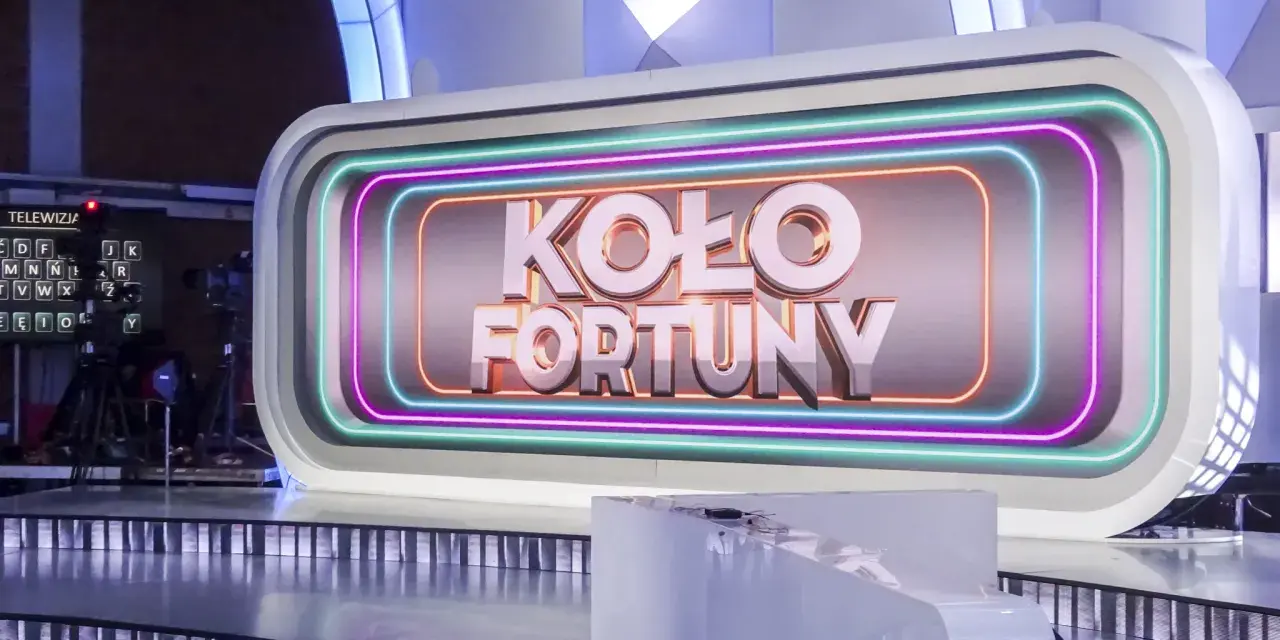 Na scenie studia telewizyjnego widnieje napis "KOŁO FORTUNY" otoczony neonami. To miejsce, gdzie marzenia o wygranej stają się rzeczywistością.