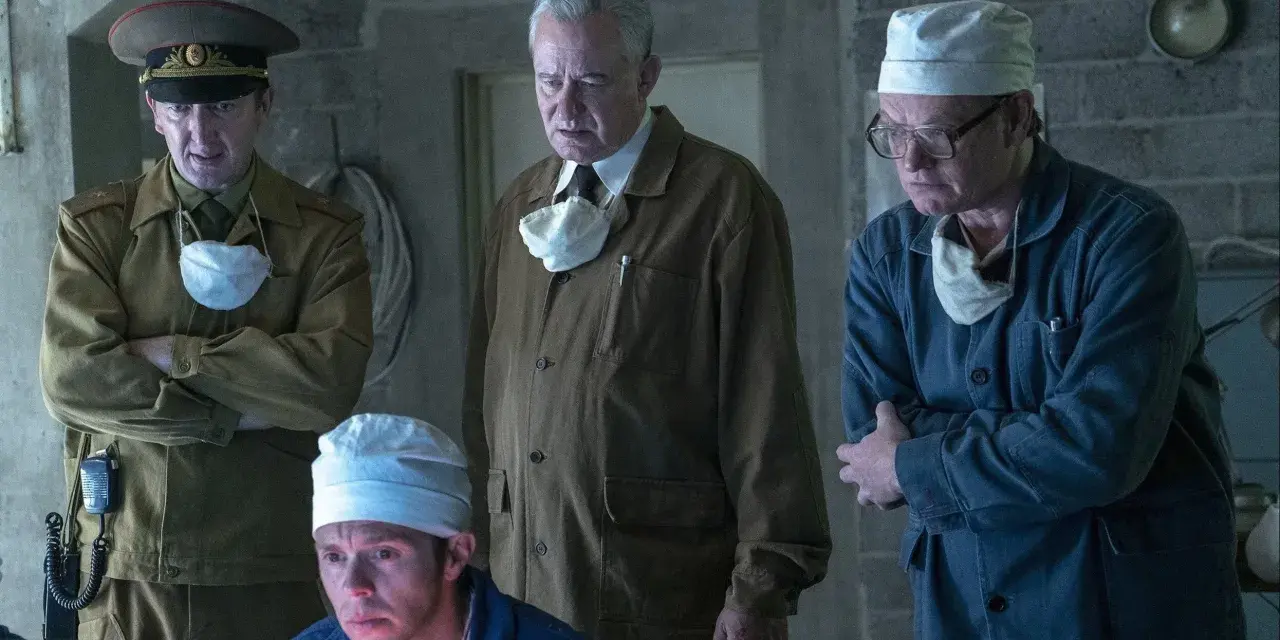 Mężczyźni w mundurach i fartuchach, w tym jeden w wojskowym, analizują coś na ekranie. Scena z serialu Czarnobyl Netflix.