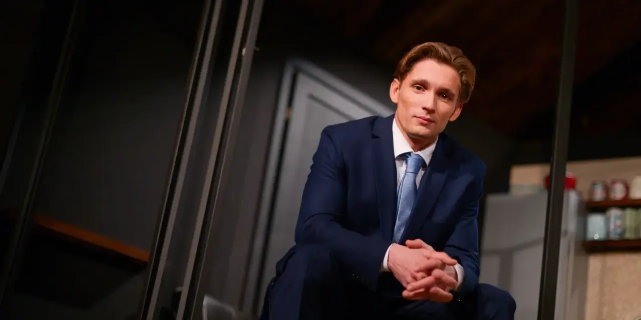 Filip Gurłacz w garniturze, siedzi na schodach, zastanawiając się, jaka to melodia.