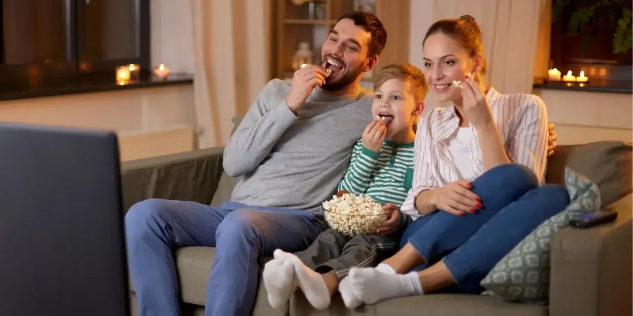 Rodzina ogląda filmy familijne, zajadając popcorn. Radość i wspólne chwile na kanapie.