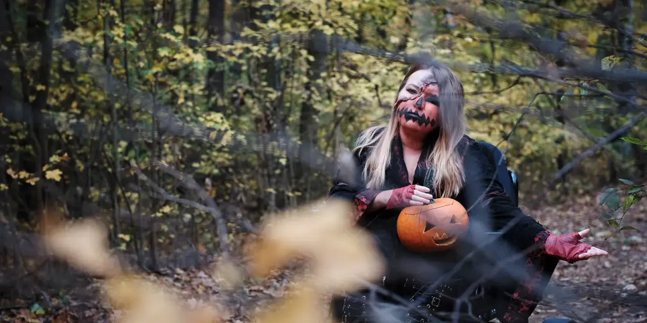 Kobieta w makijażu jack-o'-lantern trzyma dynię, gotowa na noc pełną **horrorów Netflix** w jesiennym lesie.