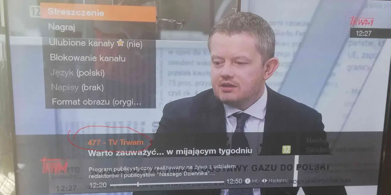 Mężczyzna w garniturze na ekranie telewizora, na którym widać menu z opcją "477 - TV Trwam".