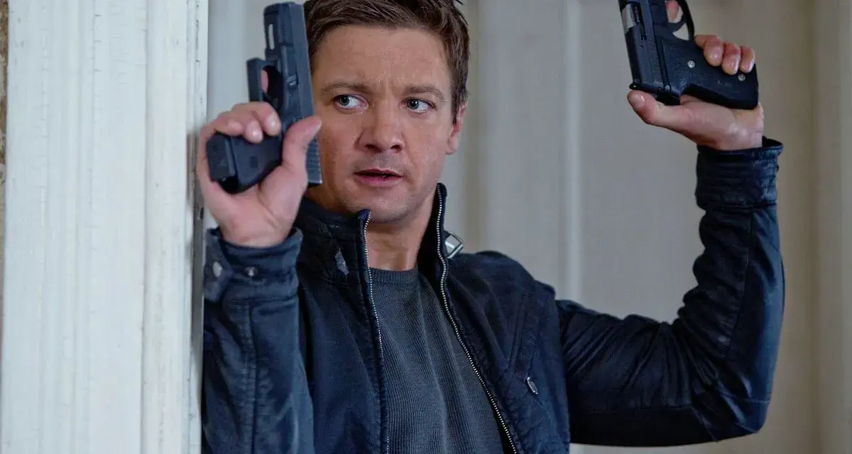 Jeremy Renner w akcji, jakiego znamy z jego filmów i seriali. W rękach trzyma dwa pistolety, gotowy do strzału.