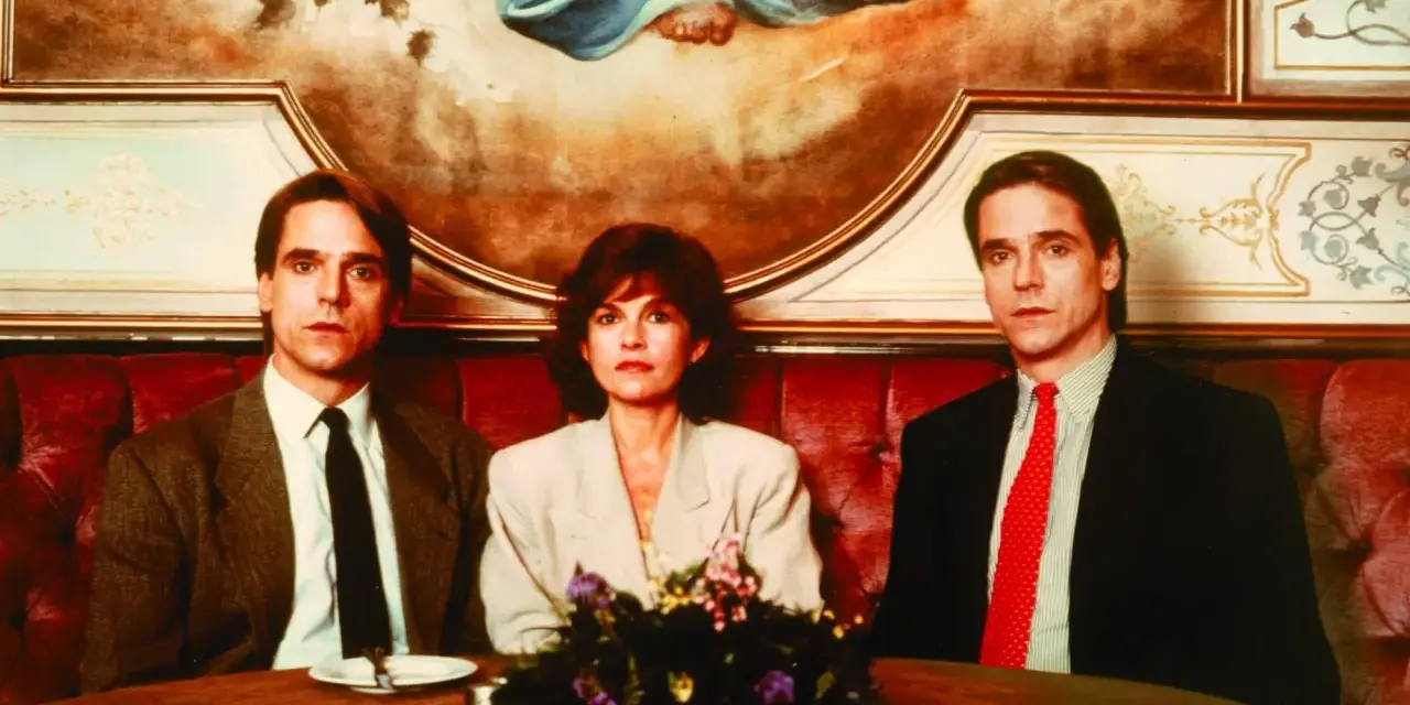 Jeremy Irons w filmach, tutaj z dwiema kobietami, siedzi przy stole w eleganckiej restauracji.
