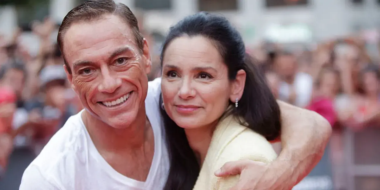 Jean-Claude Van Damme z uśmiechem obejmuje swoją żonę, Gladys Portugues, na tle tłumu.