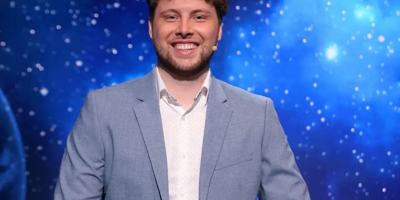Uśmiechnięty mężczyzna w jasnej marynarce, jeden z dziesięciu jak się zgłosić, na tle kosmicznego nieba.