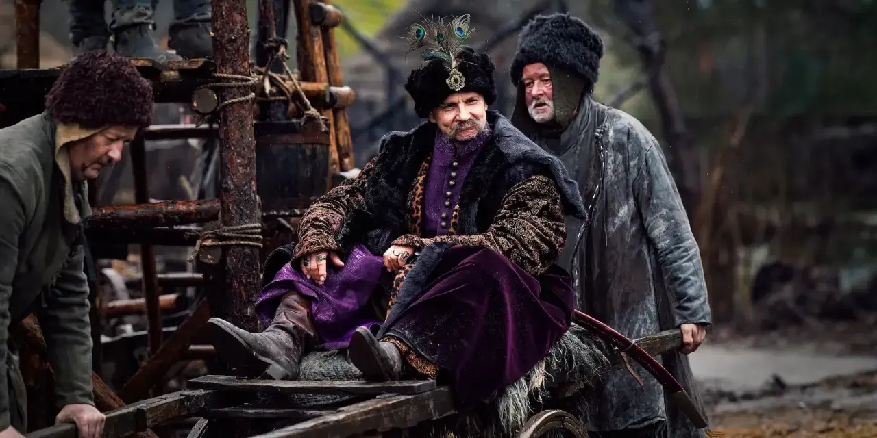 Bogaty pan w purpurowym stroju i futrzanej czapie z pawim piórem, siedzi na wozie. Czy to zapowiedź drugiego sezonu 1670?