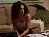 Kobieta z kręconymi włosami, w podkoszulku, siedzi na podłodze, trzymając pistolet. Scena z filmów i seriali Emmy Rossum.