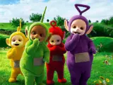 Teletubisie imiona: Tinky Winky, Dipsy, Laa-Laa i Po stoją na zielonej łące pełnej kwiatów.