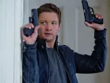 Jeremy Renner w akcji, jakiego znamy z jego filmów i seriali. W rękach trzyma dwa pistolety, gotowy do strzału.