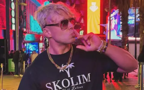Skolim w okularach i złotych łańcuchach, pozuje na tle neonów. Król Latino w swoim wieku, w blasku miasta.