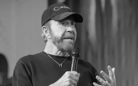 Chuck Norris, mimo swojego wieku, wciąż ma charyzmę. Mówi do mikrofonu w czapce z daszkiem.