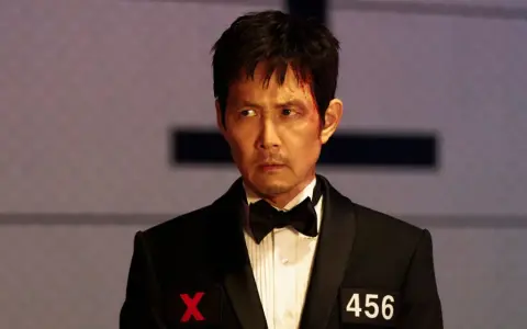 Zraniony Seong Gi-hun w garniturze z numerem 456 i symbolem X, gotowy na kolejne wyzwania w Squid Game sezon 4.