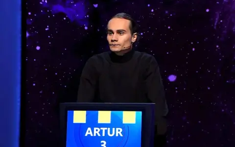 Artur, który wygrał jeden z dziesięciu, stoi na scenie w czarnym golfie.