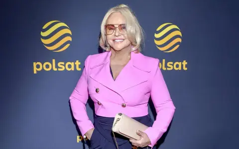 Kobieta w różowej marynarce i okularach, pozuje na tle logo Polsat. Może to być jedna z gwiazd serialu "Teściowie" w obsadzie.