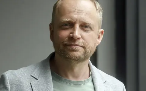 Piotr Adamczyk, znany z wielu filmów, seriali i programów, w jasnej marynarce i zielonej koszulce.