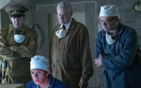 Mężczyźni w mundurach i fartuchach, w tym jeden w wojskowym, analizują coś na ekranie. Scena z serialu Czarnobyl Netflix.