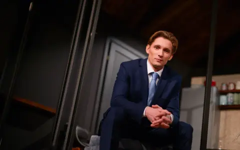 Filip Gurłacz w garniturze, siedzi na schodach, zastanawiając się, jaka to melodia.