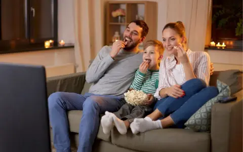 Rodzina ogląda filmy familijne, zajadając popcorn. Radość i wspólne chwile na kanapie.