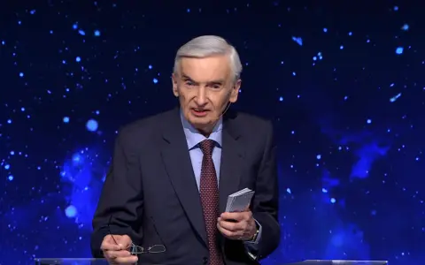 Stars twinkle behind a man in a suit, holding glasses and a small book. He looks like he's been on "Jeden z dziesięciu" for a long time.