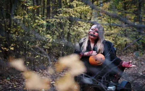 Kobieta w makijażu jack-o'-lantern trzyma dynię, gotowa na noc pełną **horrorów Netflix** w jesiennym lesie.
