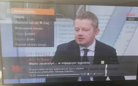 Mężczyzna w garniturze na ekranie telewizora, na którym widać menu z opcją "477 - TV Trwam".