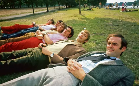 Grupa mężczyzn w kolorowych spodniach leży na trawie, jakby szykowali się do sceny z Monty Pythona.