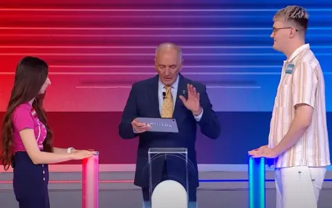 Na planie Familiady, prowadzący trzyma tablet z napisem "FAMILIADA". Po bokach stoją uczestnicy.