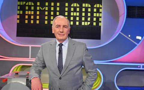 Mężczyzna w garniturze na tle planszy teleturniejowej, wyglądający na siłach i gotowy do gry, by być zdrowym jak Familiada.