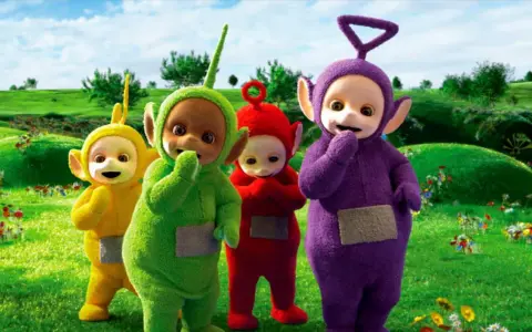 Teletubisie imiona: Tinky Winky, Dipsy, Laa-Laa i Po stoją na zielonej łące pełnej kwiatów.