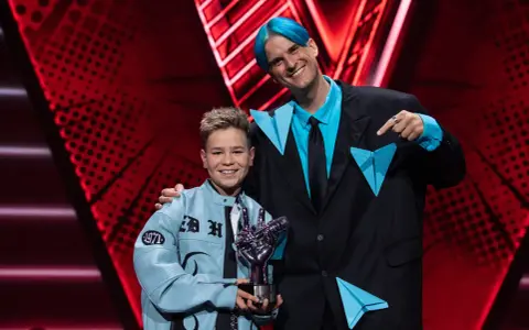 Chłopiec z błękitną kurtką i trofeum w kształcie dłoni, obok mężczyzny z niebieskimi włosami. To on wygrał The Voice Kids!