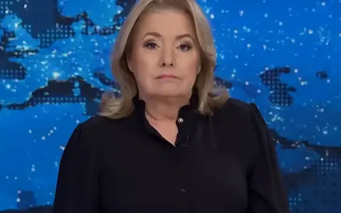 Kobieta w czarnej bluzce na tle mapy świata. Jej poważna mina sugeruje, że omawia ważne wiadomości, które wpływają na oglądalność.